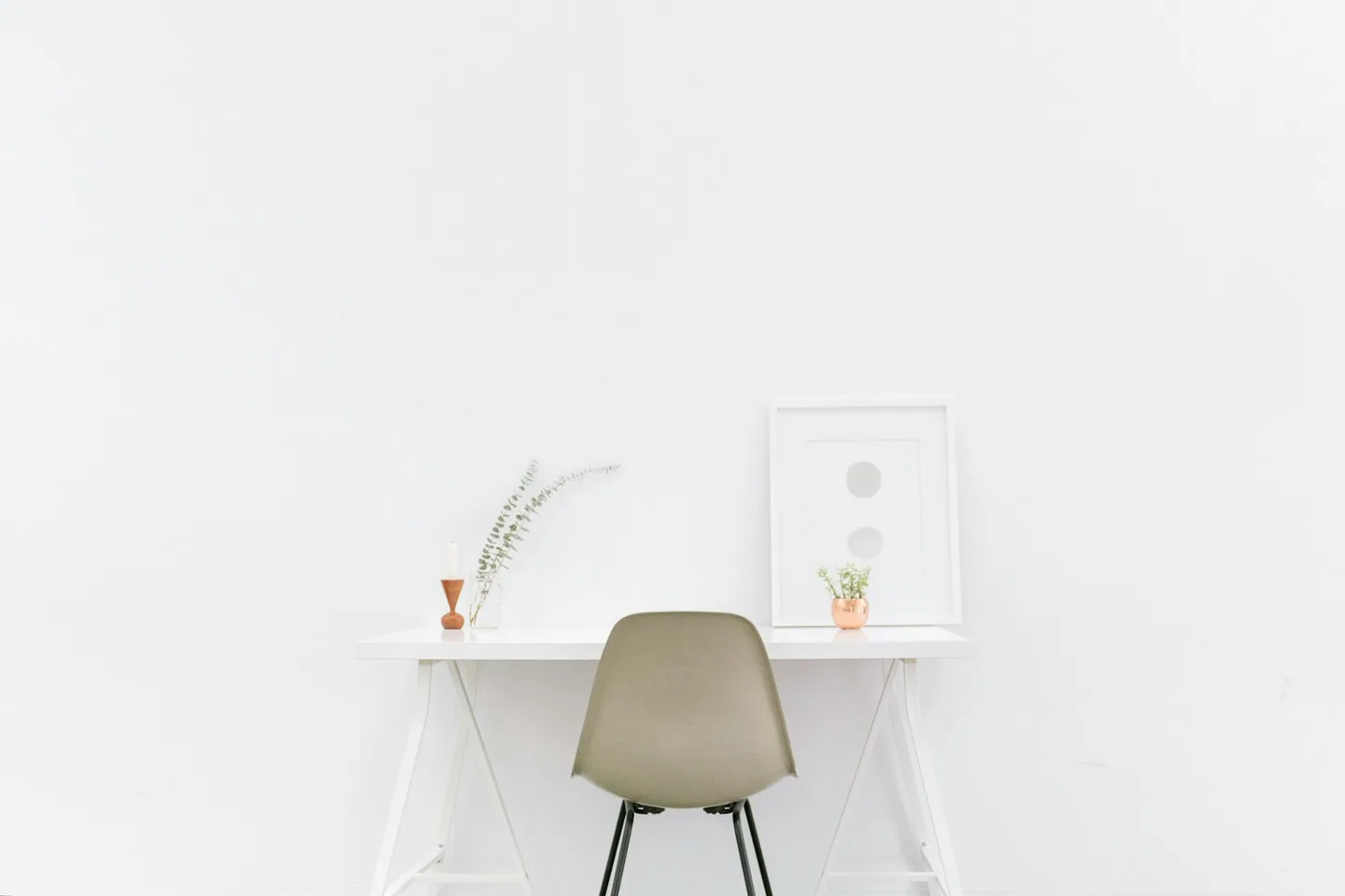 Minimal white desk with a pale chair, small plants, and a vase against a white wall