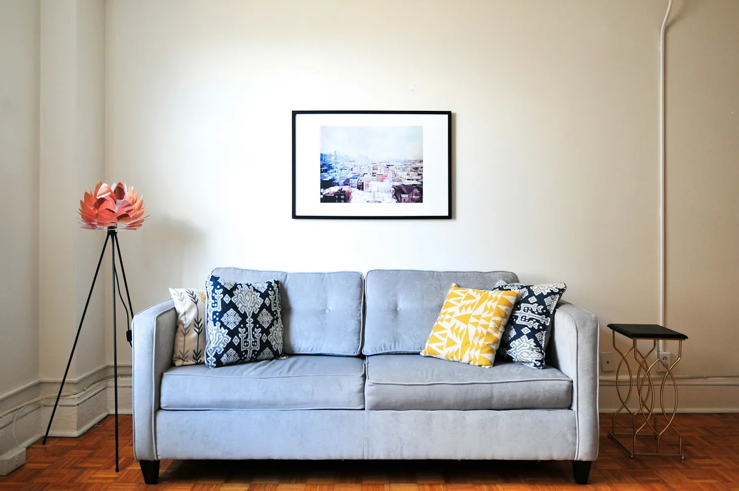 A pale blue sofa with patterned cushions beside a small table and framed wall art