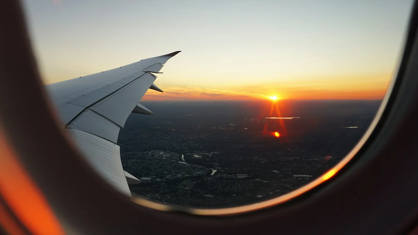 A view through an airplane window toward a wing at sunset